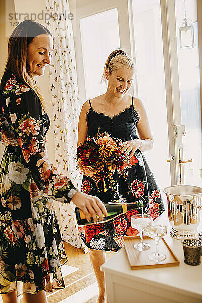 Lächelnde Frau serviert Champagner in einem Trinkglas  während sie neben einem Freund steht