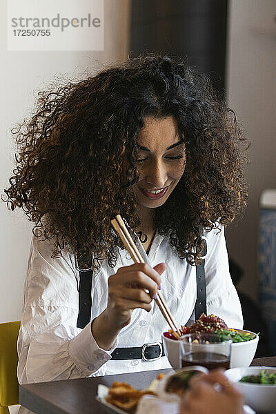 Junge Frau mit lockigem Haar beim Essen im Restaurant