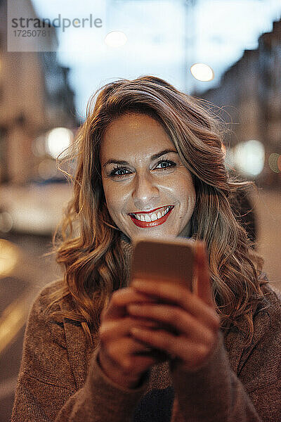 Mittlere erwachsene Frau lächelt und hält ein Smartphone