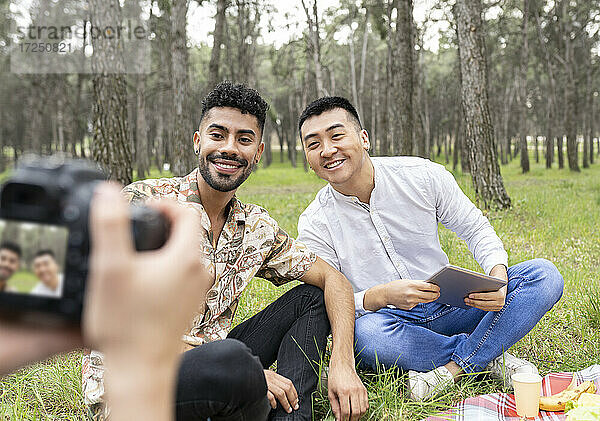 Frau fotografiert männliche Freunde  die während einer Party im Wald sitzen