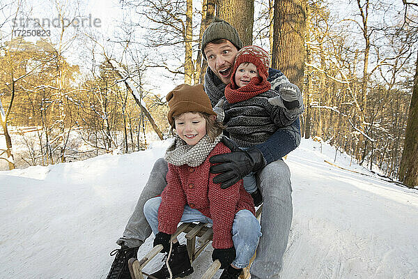 Verspielter Vater hält seine Söhne beim Schlittenfahren auf Schnee im Winter