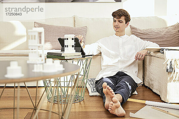 Männlicher Architekt mit digitalem Tisch vor dem Sofa zu Hause