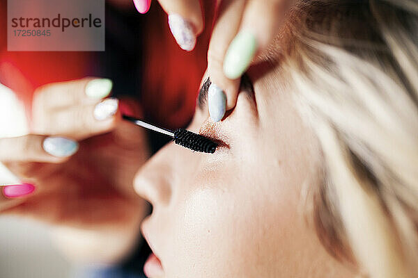 Eine Visagistin trägt im Studio Mascara auf die Wimpern eines Models auf
