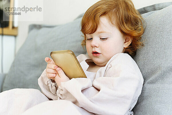 Nettes rothaariges Mädchen benutzt Handy auf Sofa im Wohnzimmer