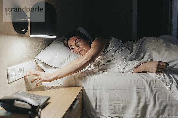 Mittlere erwachsene Frau schaltet das Licht aus  während sie auf dem Bett liegt