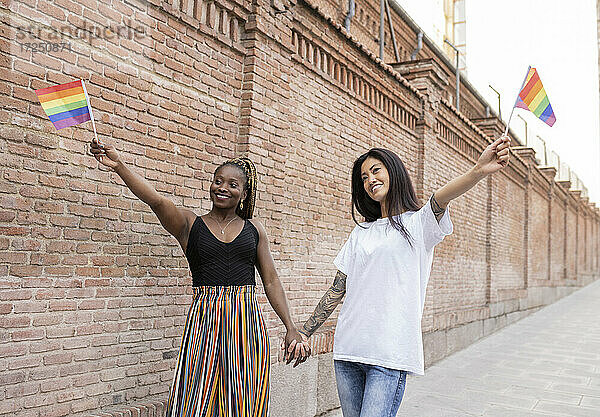 Multiethnisches lesbisches Paar hält Flagge  während es auf dem Fußweg nahe der Mauer steht