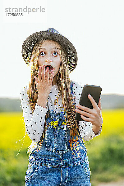 Schockiertes Mädchen mit Smartphone auf einem landwirtschaftlichen Feld