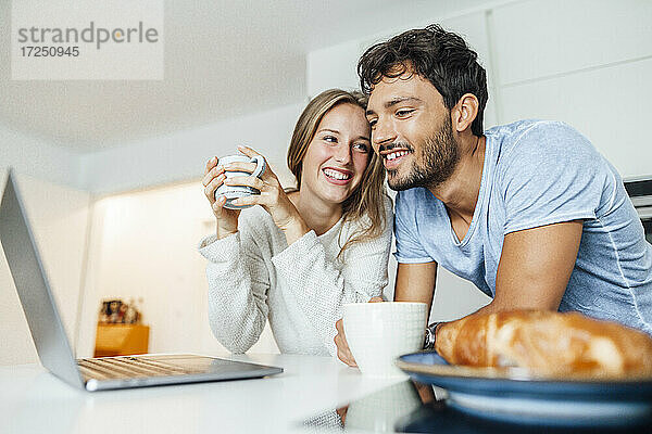 Glückliches junges Paar trinkt Kaffee und lehnt sich dabei an den Küchentisch zu Hause