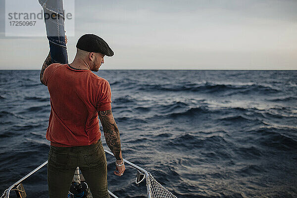 Hipster-Mann schaut weg  während er im Urlaub auf einem Boot im Meer steht
