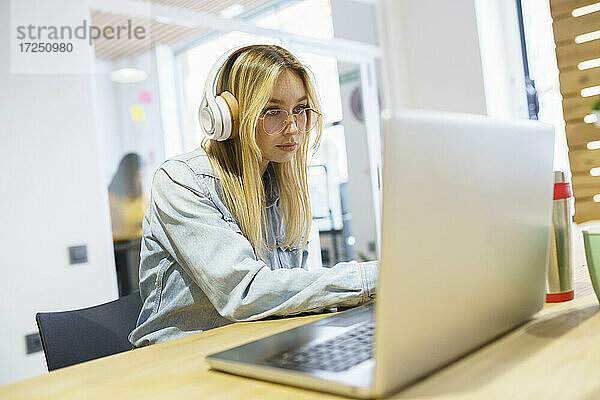 Blonde Geschäftsfrau mit Laptop und Kopfhörern im Büro