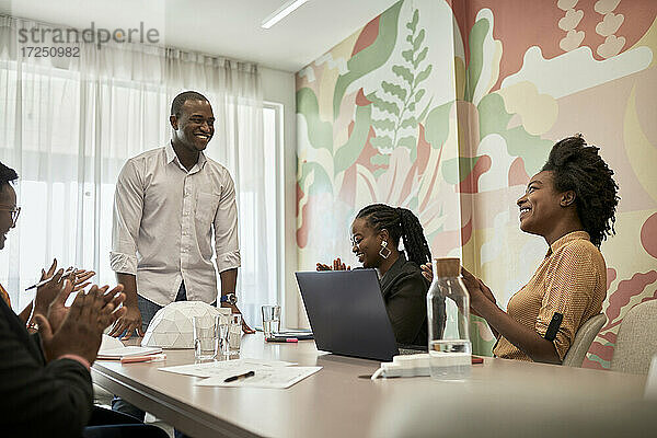 Lächelnder männlicher Architekt  der Geschäftsleute ansieht  die während eines Treffens im Coworking-Büro klatschen