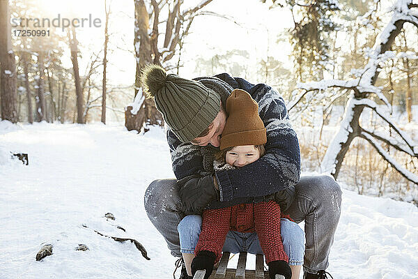 Vater umarmt seinen Sohn  während er im Winter auf dem Schlitten sitzt