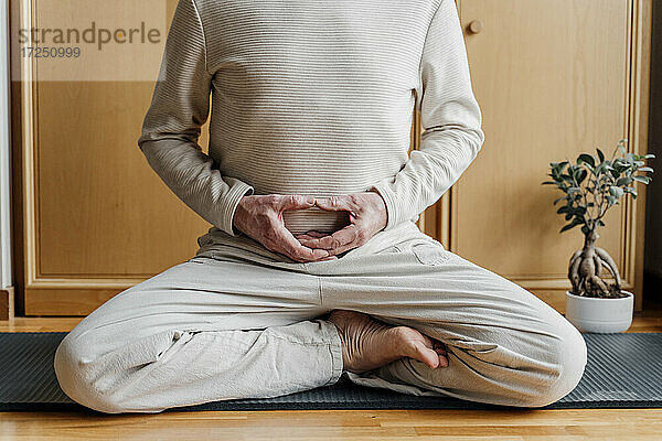 Älterer Mann macht Yoga im Schneidersitz auf einer Übungsmatte