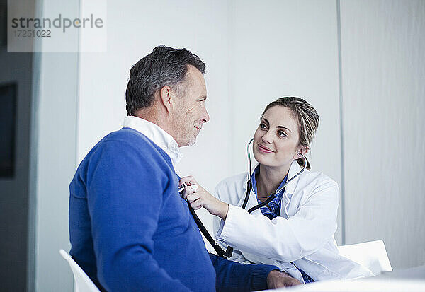 Lächelnde Ärztin  die einen männlichen Patienten mit Stethoskop im Krankenhaus untersucht