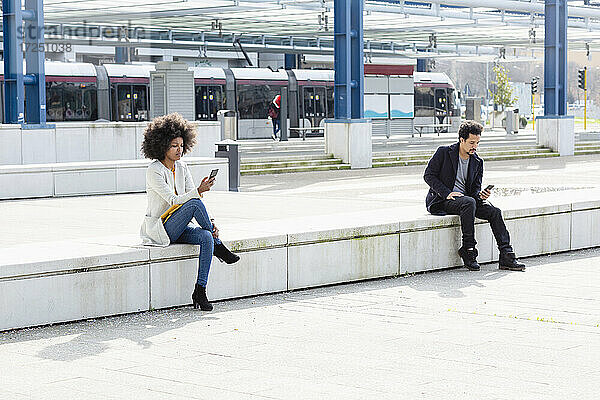 Männliche und weibliche Mitarbeiter nutzen Smartphones  während sie sich in der Nähe des Bahnhofs sozial distanzieren