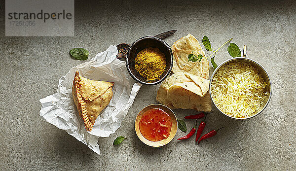 Studioaufnahme von Samosa-Knödel auf Papierserviette  Schüssel mit Basmati-Reis  Chili-Dip-Sauce  Naan-Brot und roten Chilischoten