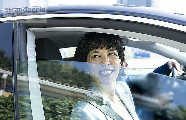 Reife Geschäftsfrau lächelt beim Blick durch das Autofenster