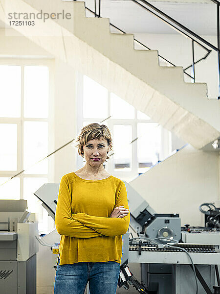 Selbstbewusste Inhaberin steht mit verschränkten Armen in der Druckwerkstatt