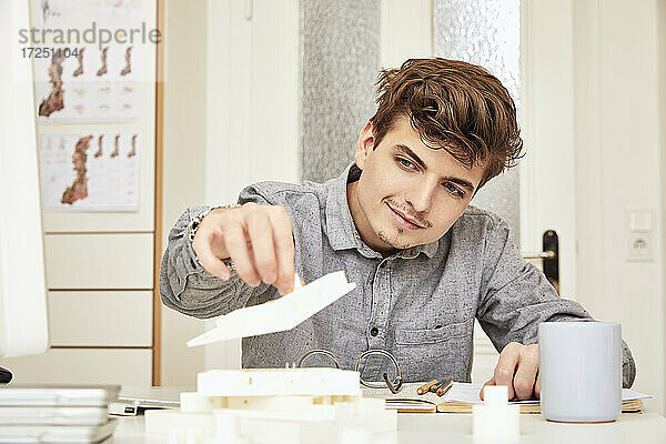 Männlicher Architekt arrangiert Modell  während er im Büro sitzt
