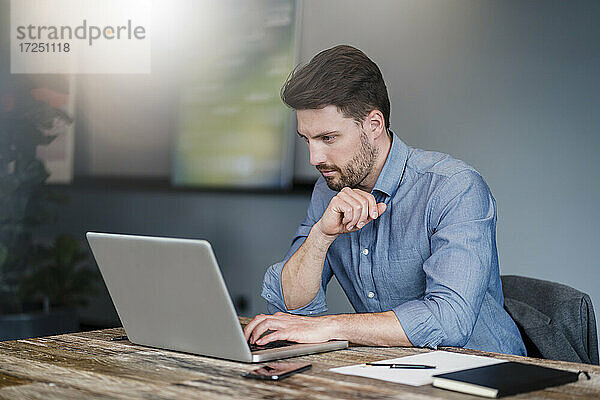 Mittlerer erwachsener männlicher Unternehmer arbeitet am Laptop über dem Tisch im Büro