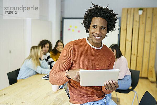 Glücklicher männlicher Berufstätiger  der ein digitales Tablet am Bürotisch benutzt