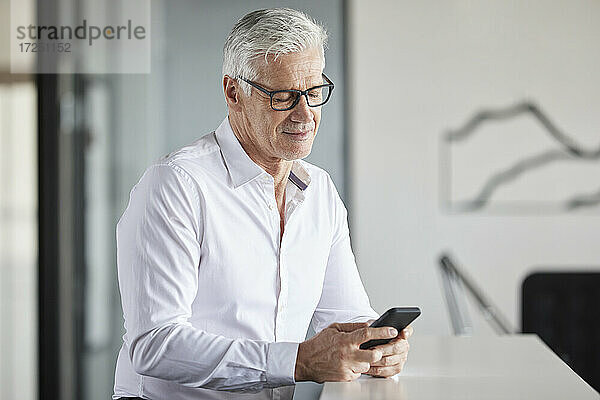 Lächelnder Unternehmer  der ein Mobiltelefon im Büro benutzt