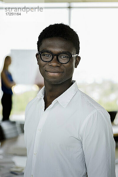 Junger männlicher Unternehmer mit Brille lächelt im Büro