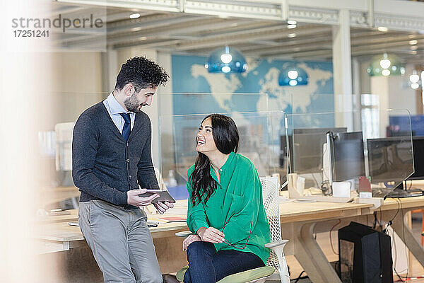 Lächelnde männliche und weibliche Unternehmer  die am Schreibtisch in einem Coworking-Büro diskutieren