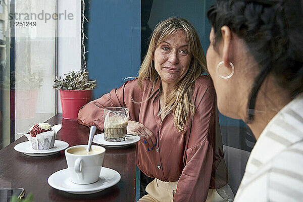 Lächelnde Frau sieht ihre Freundin an  während sie in der Cafeteria Kaffee trinkt