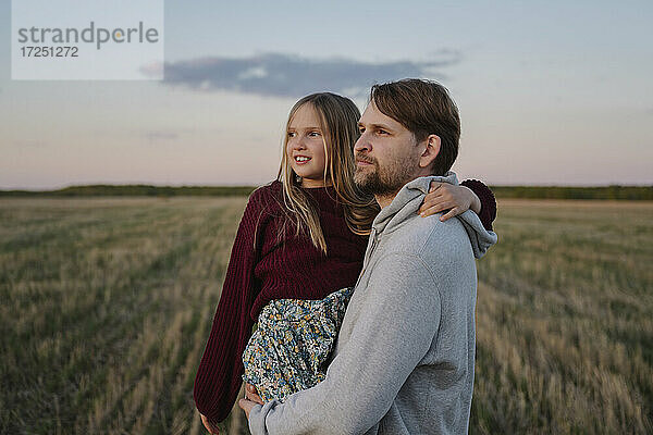 Vater mit Tochter in einem Feld stehend und Sonnenuntergang beobachtend