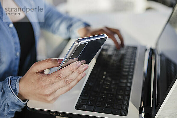 Weibliche Fachkraft  die ein Mobiltelefon hält  während sie in einem Café am Laptop arbeitet