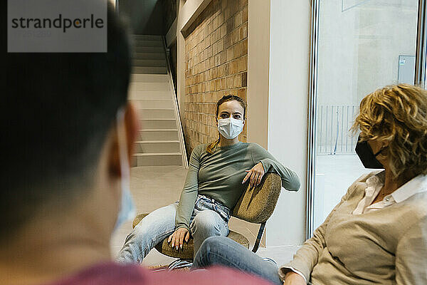 Geschäftsfrau mit Gesichtsschutzmaske diskutiert mit Kollegen in der Bürolobby während COVID-19