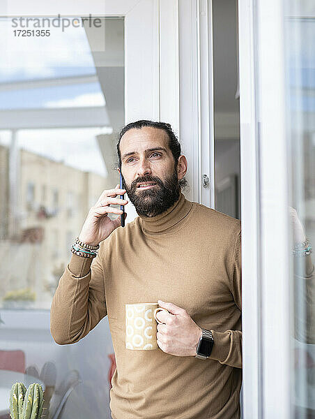 Älterer Mann spricht mit seinem Smartphone und hält eine Tasse an der Tür