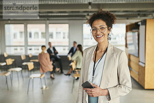 Lächelnde Geschäftsfrau mit Mobiltelefon im Konferenzzentrum