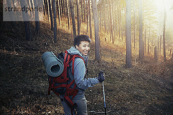 Lächelnde Frau mit Rucksack schaut über die Schulter beim Wandern im Wald
