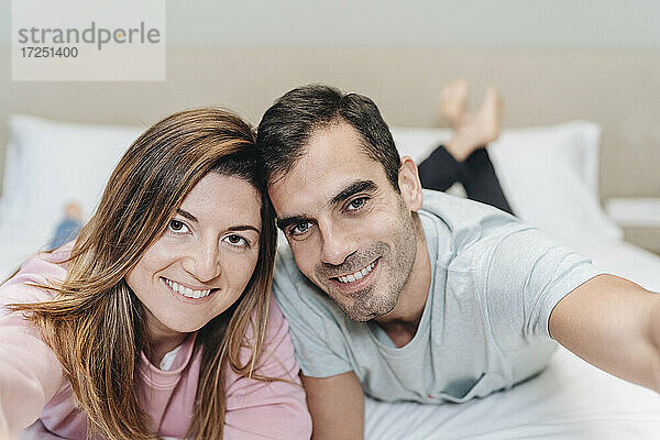 Lächelndes Paar  das zusammen auf einem Bett in einem Hotelzimmer liegt