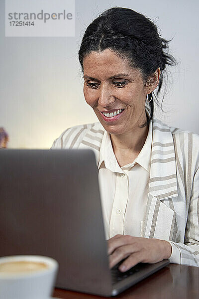 Lächelnde weibliche Fachkraft  die in der Cafeteria am Laptop arbeitet