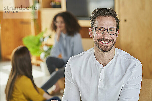 Lächelnder männlicher Unternehmer mit Kollegen im Hintergrund im Kreativbüro