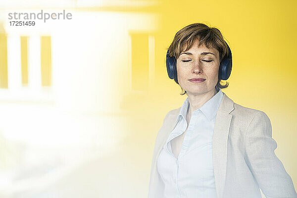 Nachdenkliche Geschäftsfrau mit Kopfhörern vor einer gelben Wand