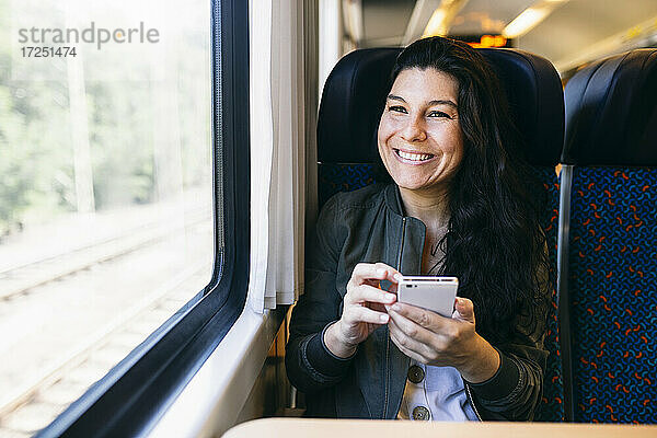 Frau mit Mobiltelefon  die im Zug sitzend durch das Fenster schaut