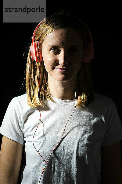 Lächelnde Frau mit Kopfhörern vor schwarzem Hintergrund