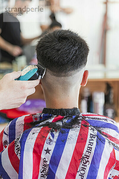 Männlicher Friseur benutzt eine Maschine  um die Frisur eines Teenagers zu stylen