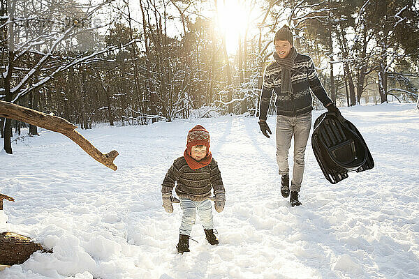 Vater mit Schlitten geht im Winter auf Schnee auf seinen Sohn zu
