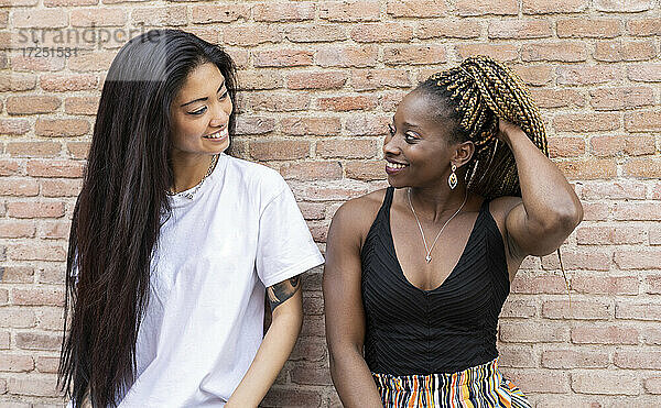Afrikanische Frau mit Hand im Haar  die ihre Freundin an der Wand betrachtet