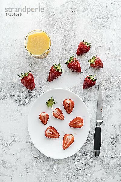 Glas Orangensaft  Küchenmesser und Teller mit frischen Erdbeeren liegen auf weißem Marmor