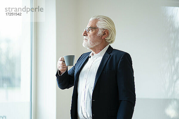Geschäftsmann mit grauem Haar hält Kaffeetasse im Büro