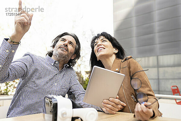 Geschäftsmann mit digitalem Tablet  der auf einen Kollegen zeigt  während er auf der Terrasse sitzt