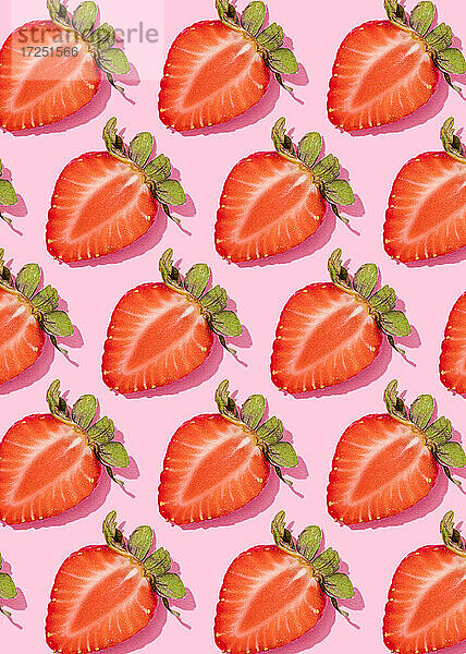 Muster von Reihen frischer halbierter Erdbeeren vor rosa Hintergrund