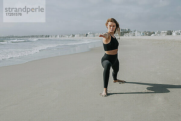 Schöne Frau übt Yoga am Strand an einem sonnigen Tag