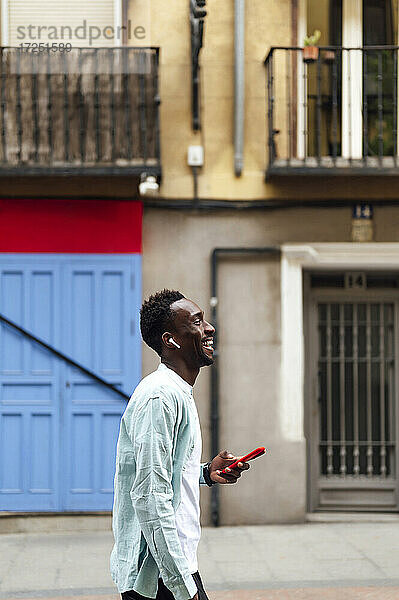 Junger Mann mit Smartphone und In-Ear-Kopfhörern auf der Straße
